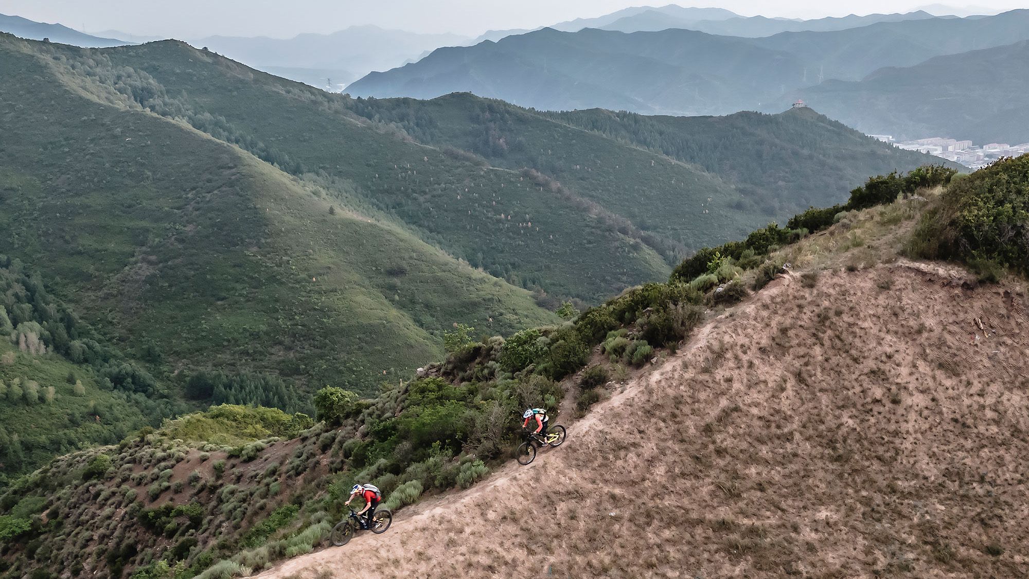 Zwei Mountainbiker auf einem Kammweg mit einer chinesischen Stadt im Hintergrund