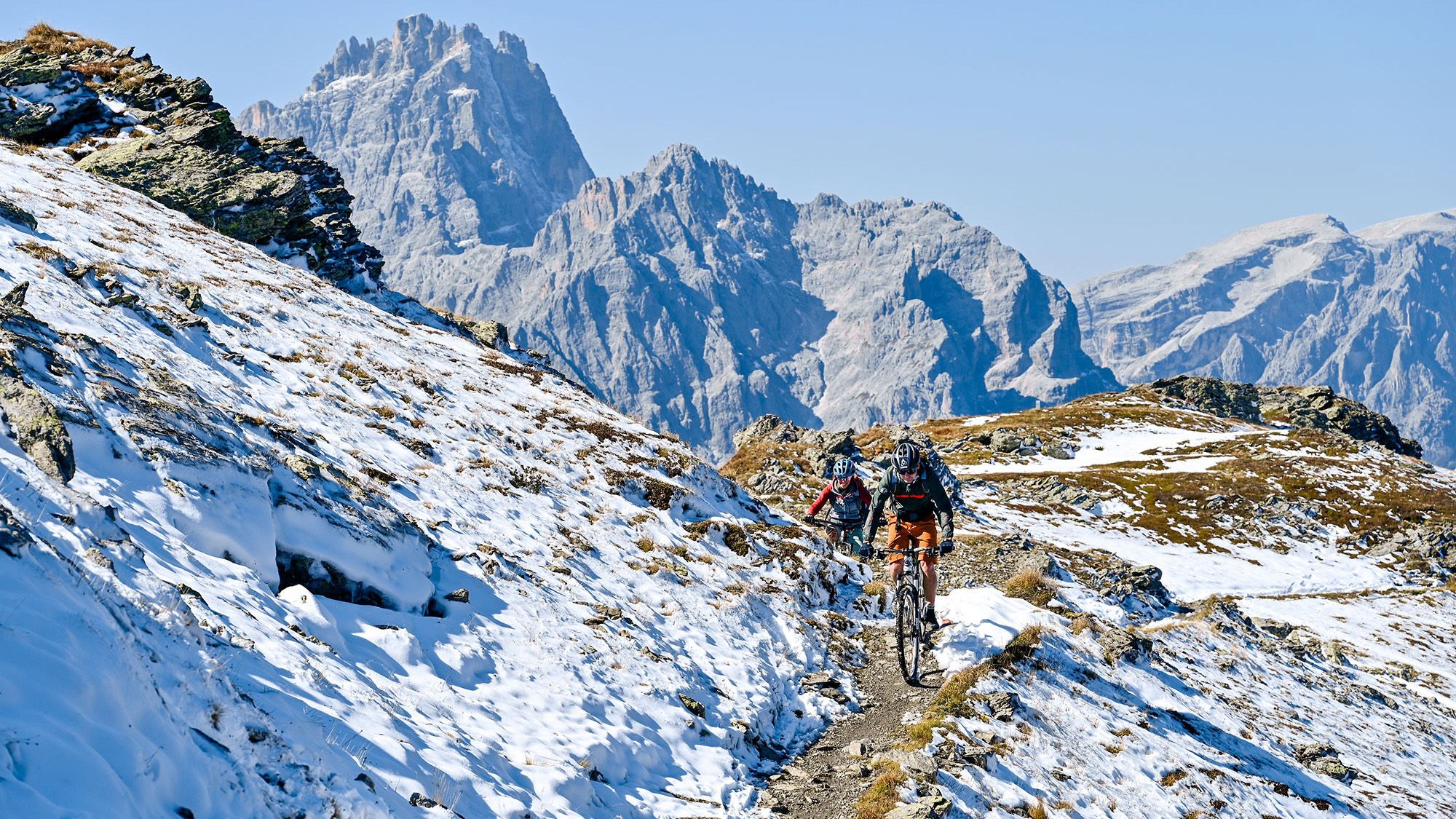 Zwei Mountainbiker auf einem Trail, der von Schnee bedeckt ist.